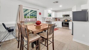 A modern kitchen with white cabinets, a wooden dining table, and a red decorative bowl.