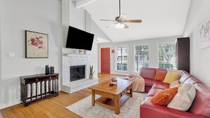 A spacious living room with a fireplace, a red sofa, a wooden coffee table, and a ceiling fan.