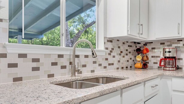A modern kitchen with a double sink, white cabinets, a coffee maker, and a backsplash with square tiles.