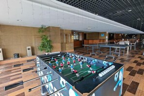 A foosball table in a hotel lobby with a checkered floor, a plant, and a seating area in the background. - Meetsuite at Kota Kinabalu (Kota Kinabalu)