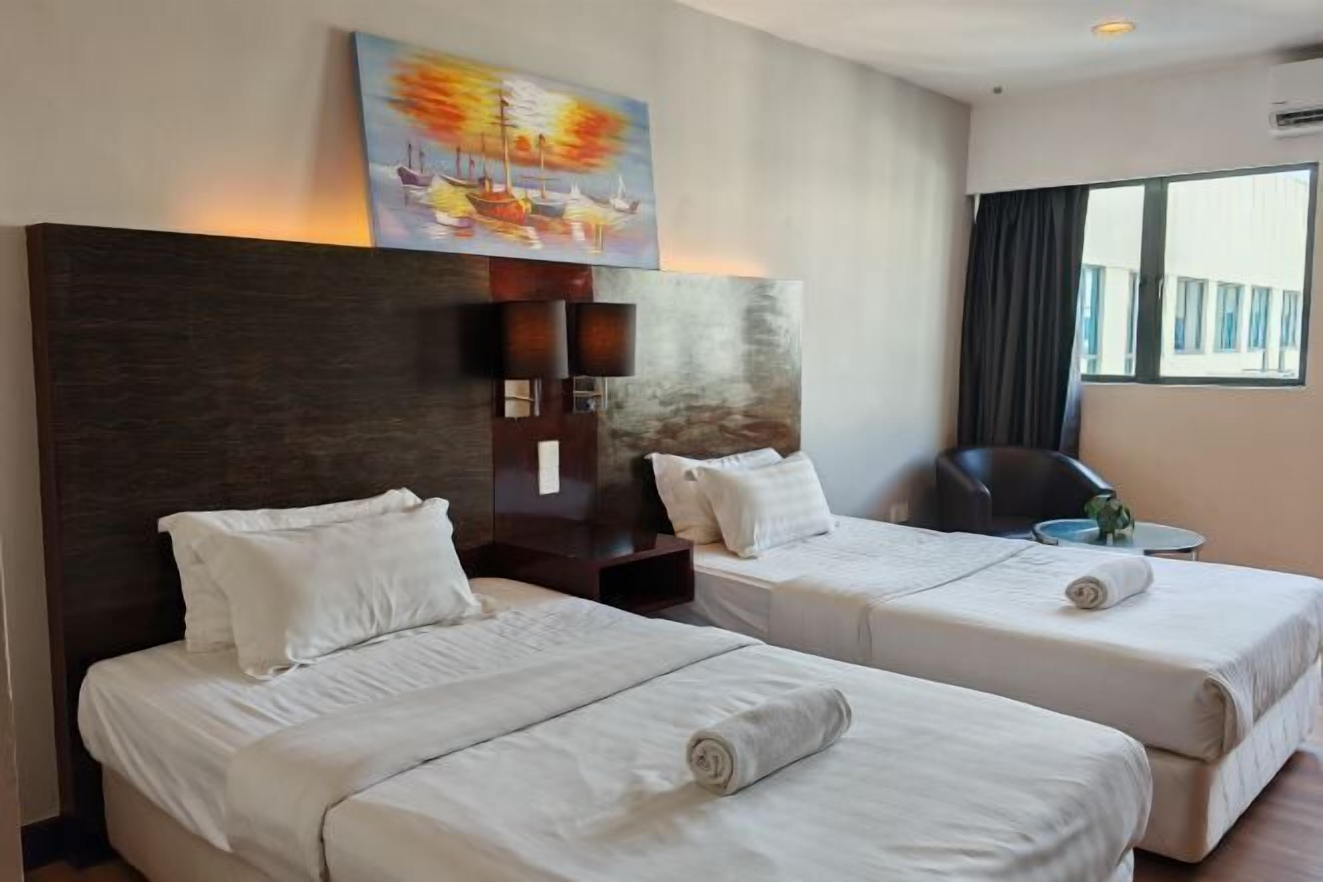 Ein Hotelzimmer mit zwei Betten, einem Gemälde über der Kopfseite, einem Schreibtisch mit Stuhl und einem Fenster mit Vorhängen.