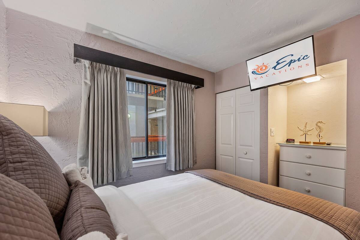 A hotel room with a bed, a dresser, a mirror, and a window with curtains.