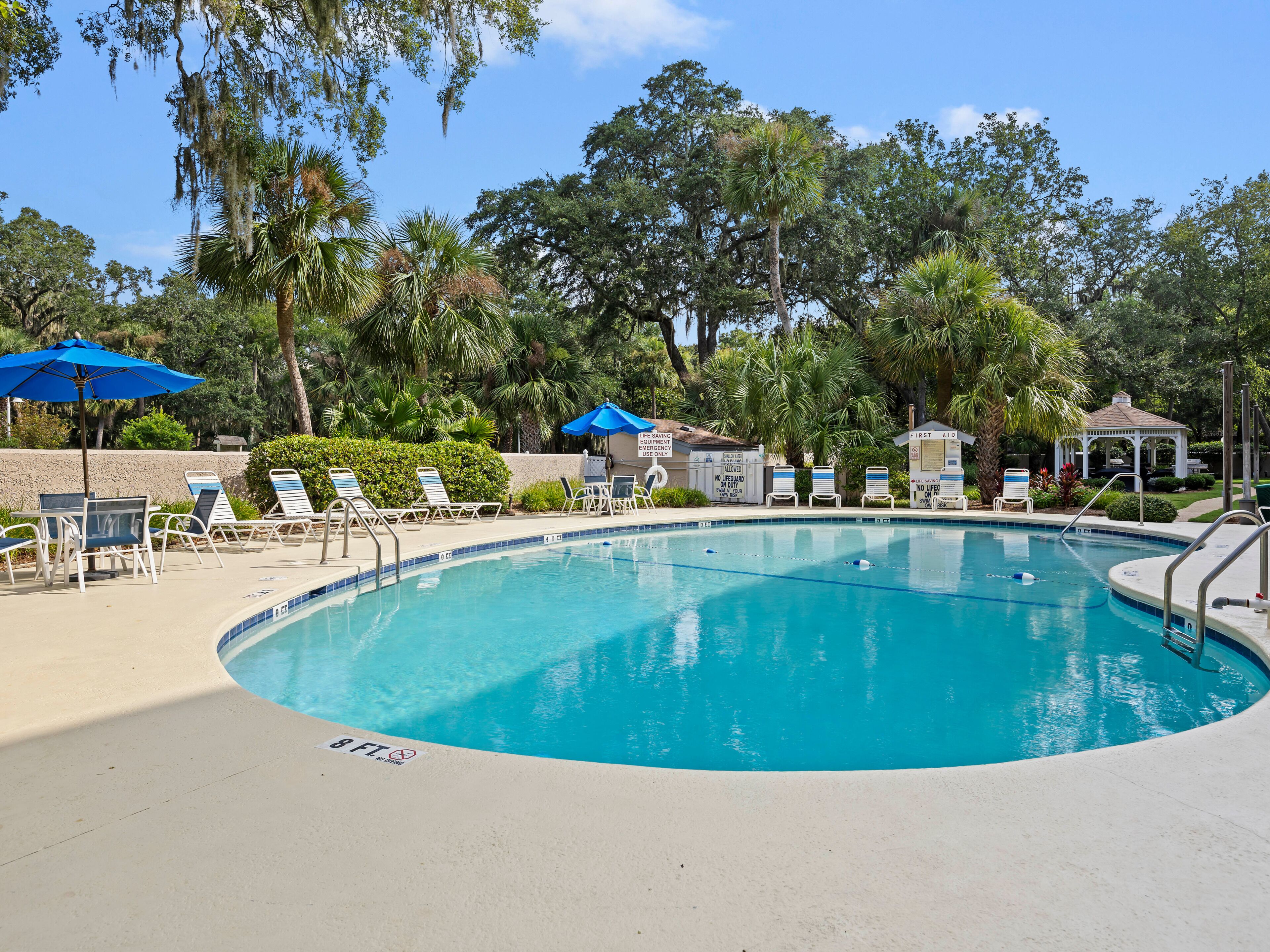 Ein Swimmingpool mit Liegestühlen und Sonnenschirmen, umgeben von Bäumen und einem Pavillon.