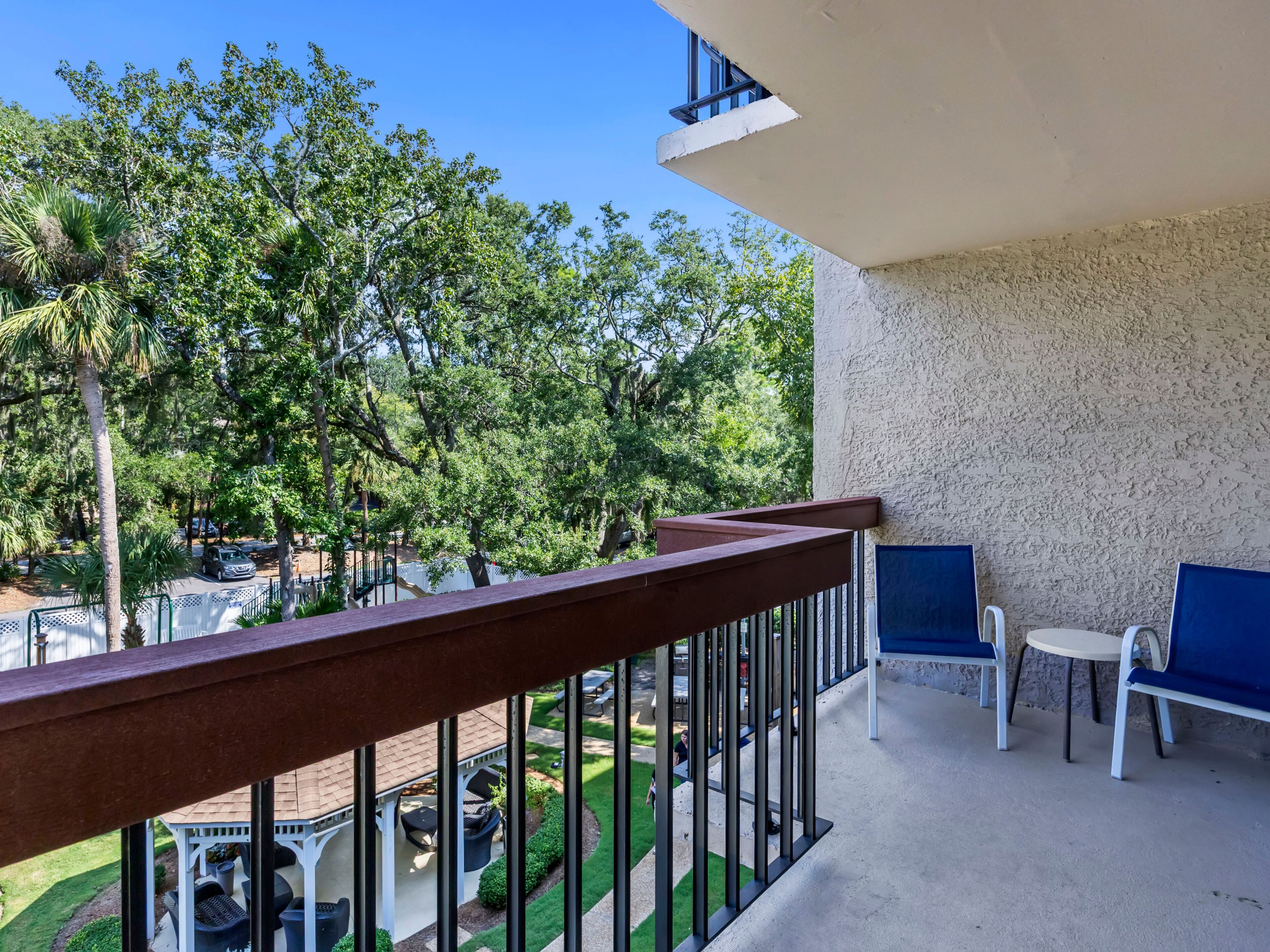 A balcony with a view of a landscaped garden and a building with a white wall and blue accents.