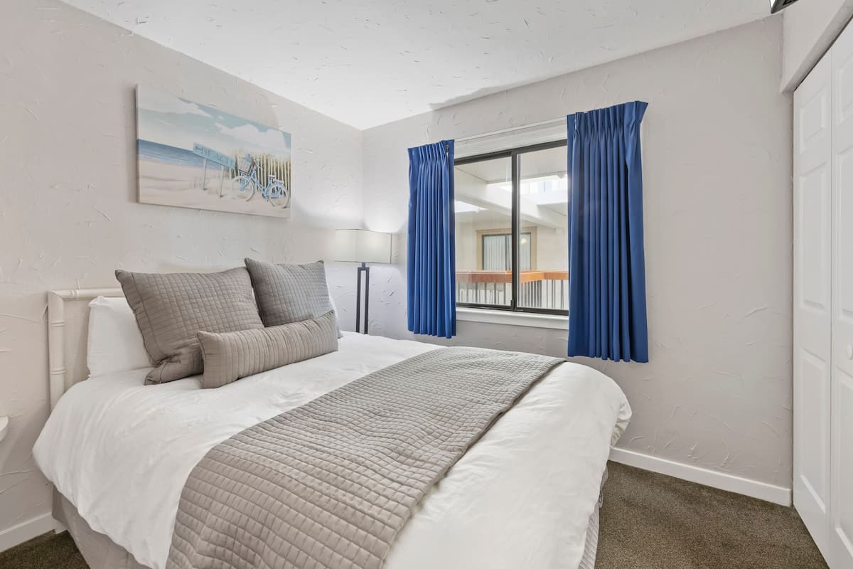 A hotel room with a bed, a painting on the wall, a window with curtains, and a view of the balcony.