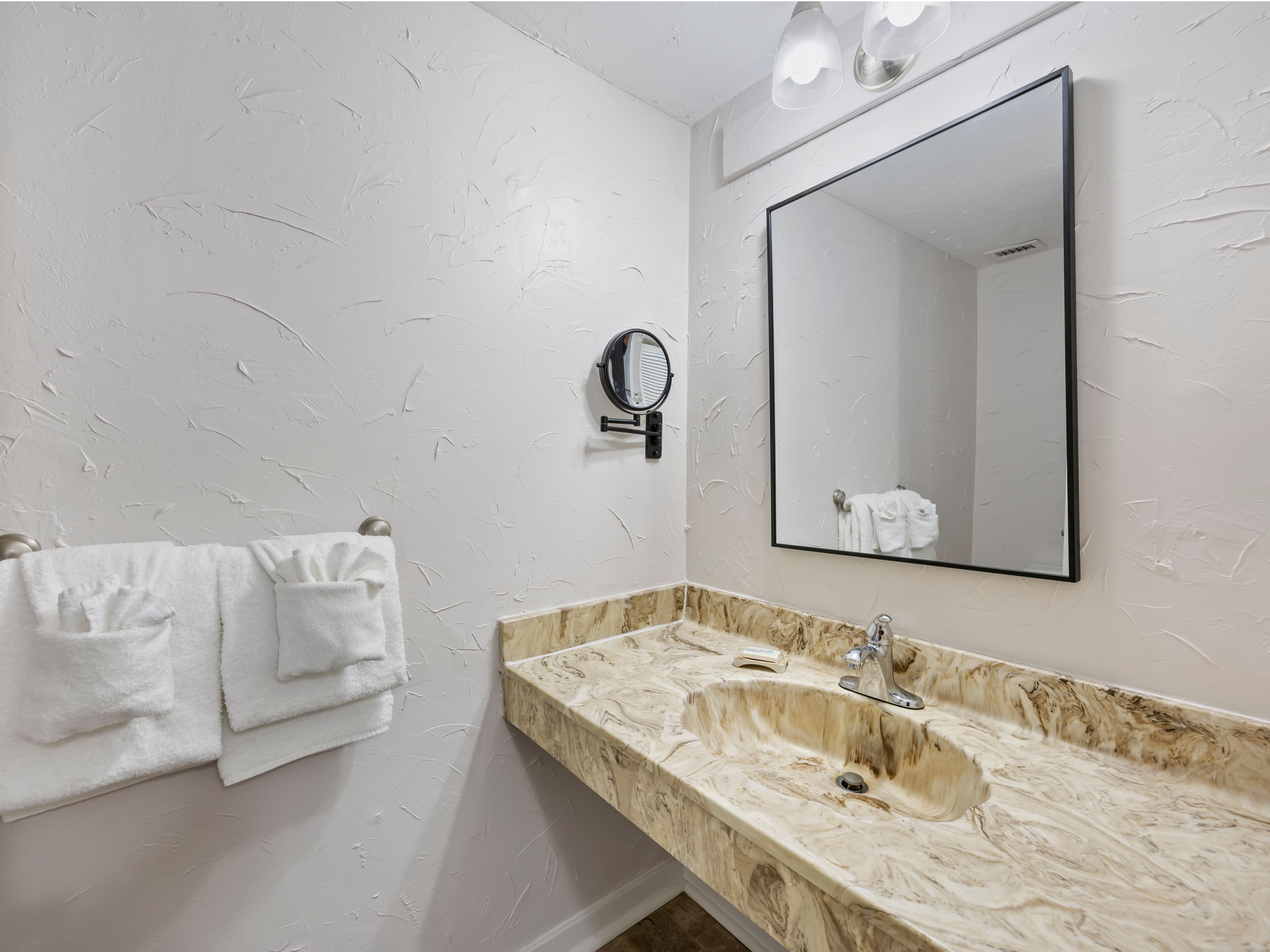 A bathroom with a marble sink, a large mirror, and a towel rack with white towels.