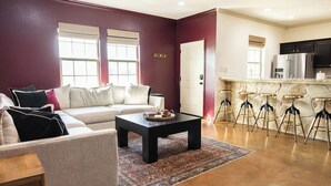 A living room with a sectional sofa, a coffee table, and a kitchen area with bar stools. - The Howdy Hangout near Texas A&M and Kyle Field (College Station)