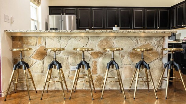 A kitchen with dark cabinets, a granite countertop, and six bar stools with gold legs. - The Howdy Hangout near Texas A&M and Kyle Field (College Station)