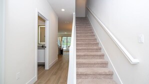 Un escalier dont les marches sont recouvertes de moquette et qui possède des rampes blanches, menant à un palier situé au deuxième étage.