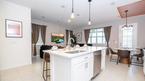 A modern kitchen with a central island, white cabinetry, and a dining area with a round table and chairs. - Chic 3BR villa Game Room close to Disney + Resort (Davenport)