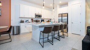 A modern kitchen with white cabinets, a central island with bar stools, stainless steel appliances, and pendant lighting. - Chic 3BR villa Game Room close to Disney + Resort (Davenport)