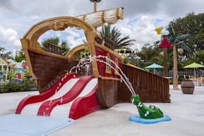A pirate-themed water play area with a slide, ship structure, and a frog statue.