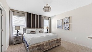 A bedroom with a wooden bed frame, two bedside tables with lamps, a ceiling light, and three framed pictures on the wall. - Entire House Davenport ~ Pool ~ Resort Access (Davenport)