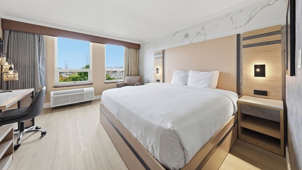 Une chambre d’hôtel avec un grand lit, un bureau, une chaise et une vue sur le paysage urbain par la fenêtre.
