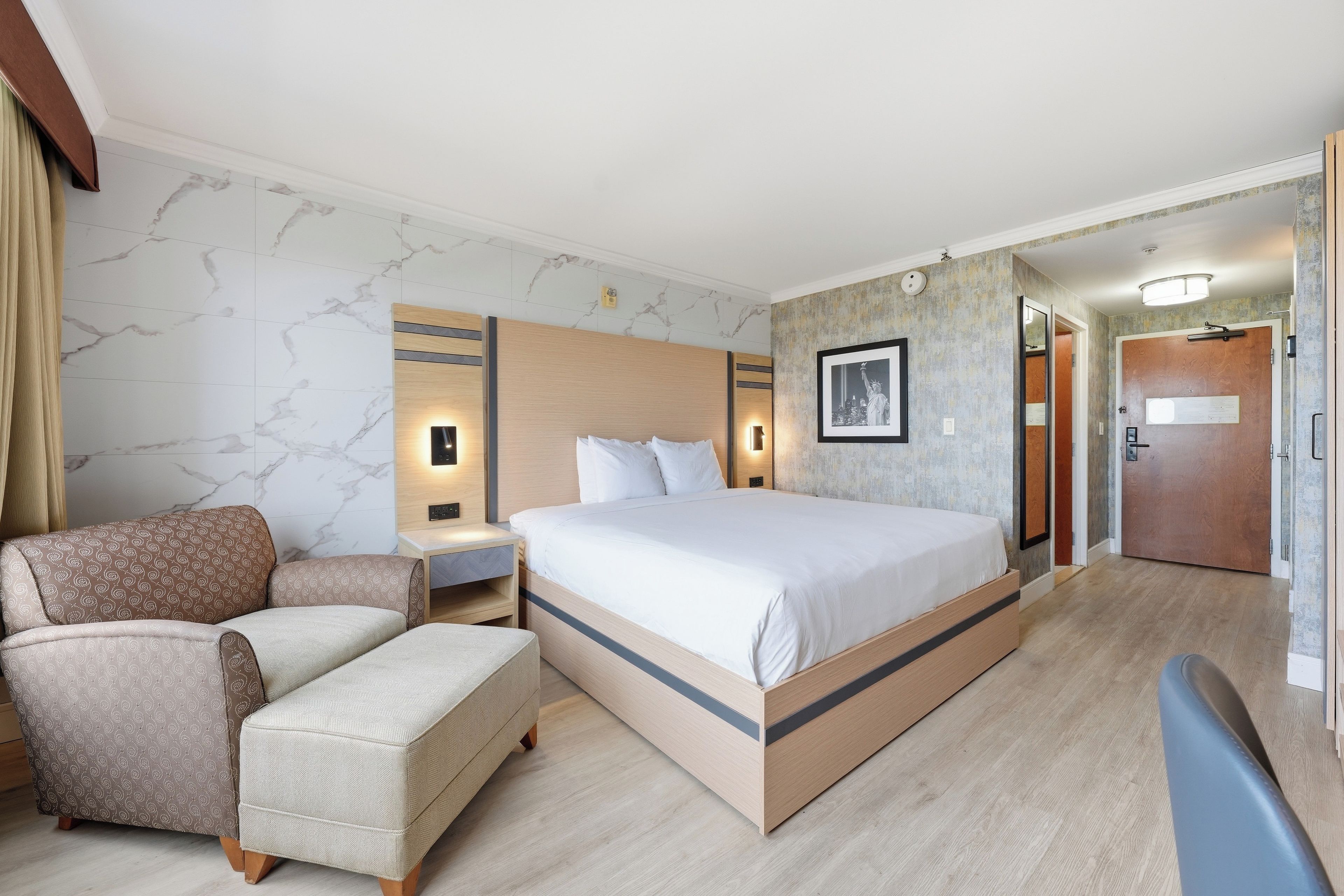 A hotel room with a bed, a chair, a desk, and a wardrobe.