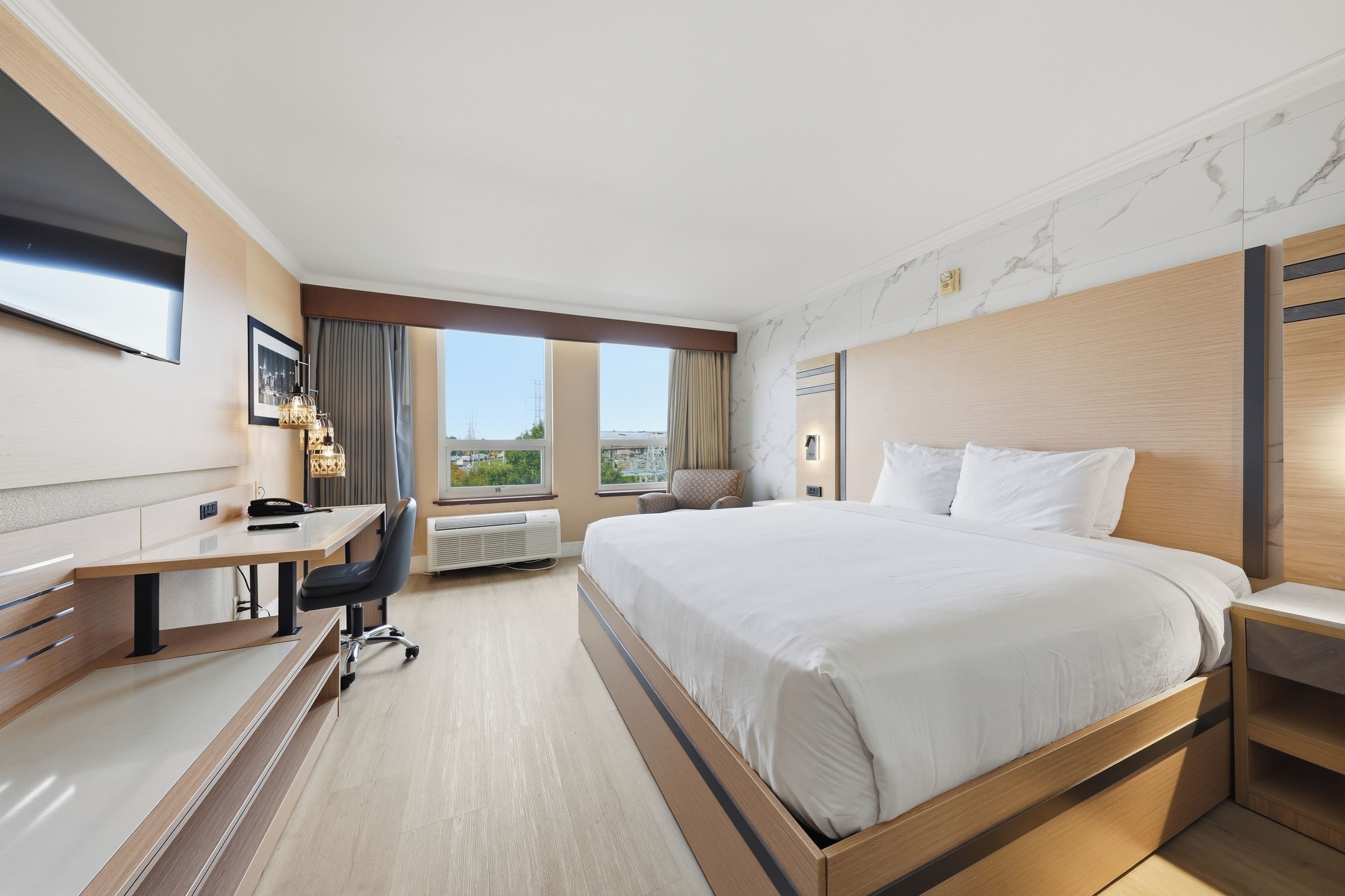 Ein Hotelzimmer mit Bett, Schreibtisch, Stuhl und Blick auf die Stadt.