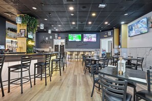 Un restaurant doté d’un bar, de plusieurs espaces pour s’asseoir et d’un écran de télévision diffusant un programme.
