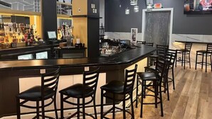 Un espace bar comprenant un comptoir, des tabourets de bar, des luminaires suspendus et un écran de télévision.
