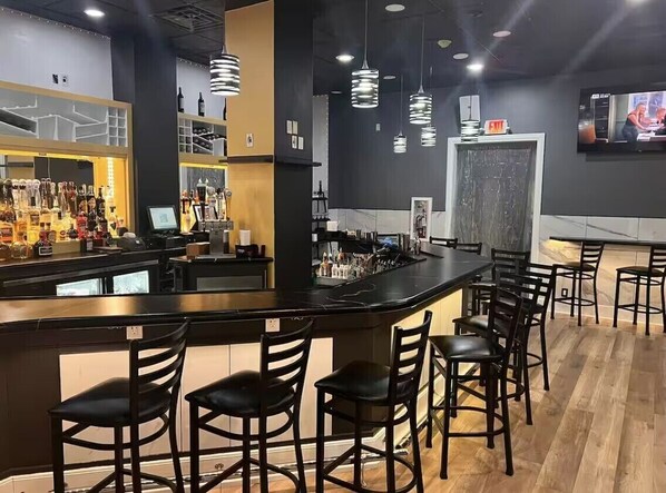 A bar area with a counter, bar stools, hanging pendant lights, and a television screen.