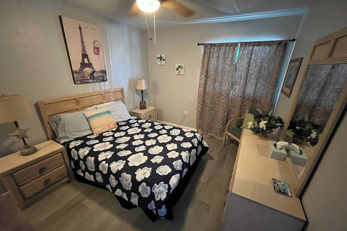 A bedroom with a bed, nightstands, a dresser, a ceiling fan, a mirror, and a window with curtains.