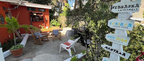 Un patio con mobiliario exterior, una antena parabólica y un cartel de madera que indica las distancias a diferentes destinos.