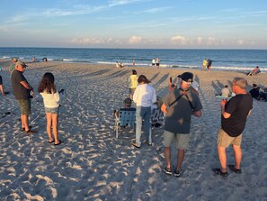 A sandy beach with people walking and sitting, a calm sea, and a clear sky. - Surfside Suites (Cocoa Beach)
