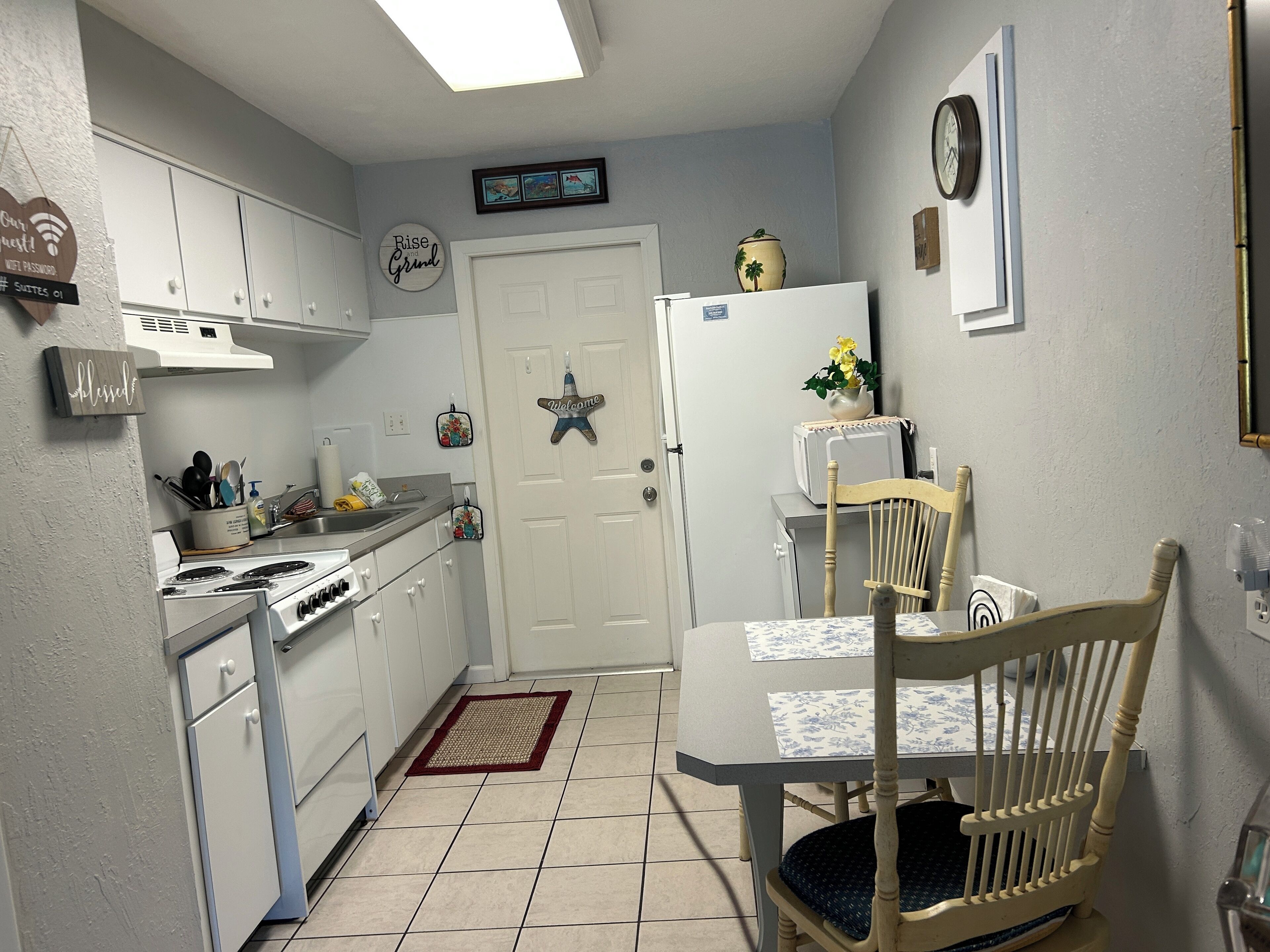 A compact kitchen with white cabinets, a stove, a refrigerator, and a dining table with a chair.