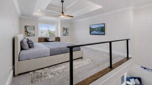 Une chambre à coucher comprenant un lit, un bureau, une chaise, un ventilateur de plafond, une fenêtre et des œuvres d’art accrochées aux murs.
