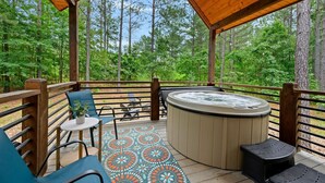 Eine überdachte Terrasse im Freien mit Whirlpool, Sitzgelegenheit und Blick auf einen Wald.