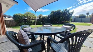 Eine Terrasse im Freien mit einem runden Tisch und Stühlen, umgeben von einem Holzzaun und Pflanzen.
