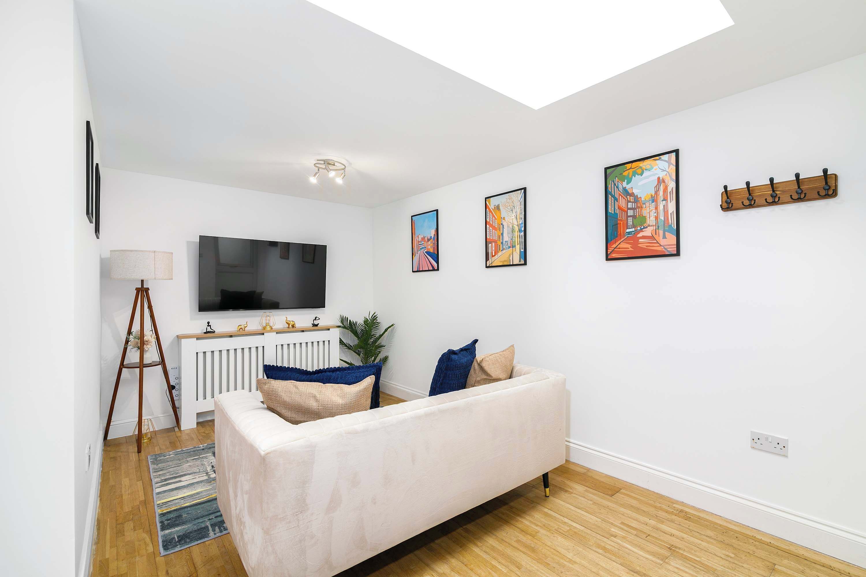 A modern living room with a sofa, a flat-screen TV, and three framed artworks on the wall.