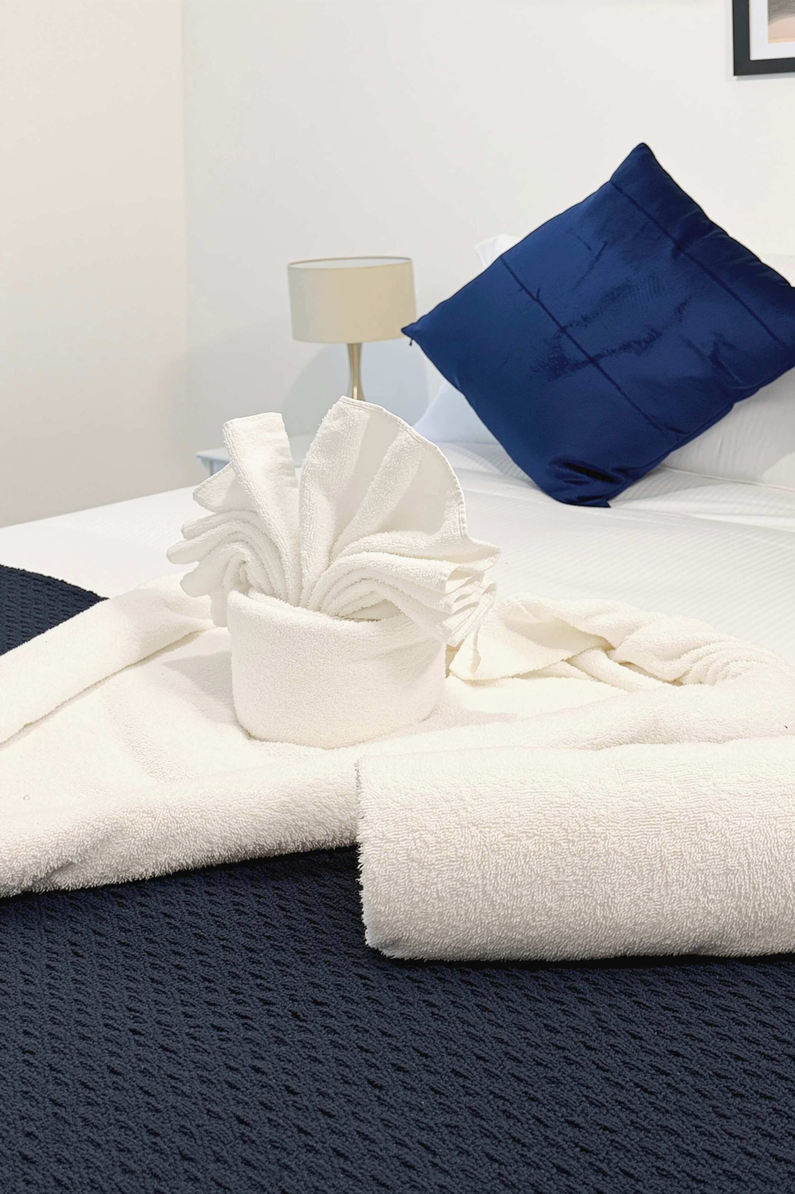 Un lit bien fait, avec une serviette blanche pliée et une composition décorative réalisée avec des serviettes blanches.