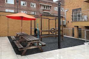 An outdoor play area with a wooden swing set, a tire swing, and a picnic table with an umbrella. - Family friendly and Modern 2BR Hoxton Shoreditch (Greater London)