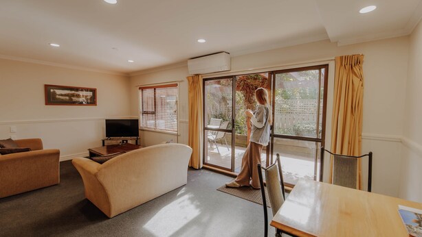 A living room with a sofa, a TV, and a table. There is a sliding glass door leading to an outdoor area. - Alpine Springs Motel | Unit 7 - HS51217 (Hanmer Springs)