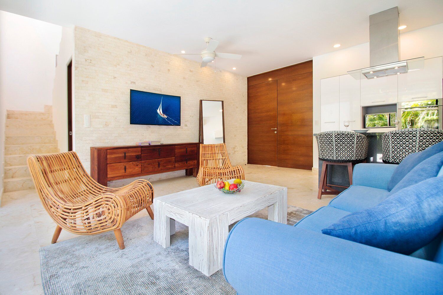 A modern living room with a white sofa, wicker chairs, a wooden cabinet, and a television on the wall.