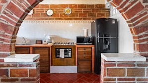 A kitchen with a brick archway, a stove, microwave, refrigerator, and a sink.