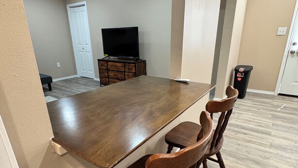 A dining area with a wooden table and chairs, a television in the background, and a trash can. - Country Nook farmhouse in San Benito (San Benito)