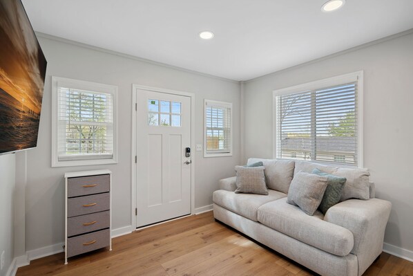 A modern living room with a beige sofa, a small white cabinet, and a door with a window. - Sunset Retreat at the Lake | Sleeps 24 | Pool & Hot Tub (Sherrills Ford)