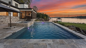 Una casa moderna con piscina, fachada de piedra y vista al lago al atardecer.