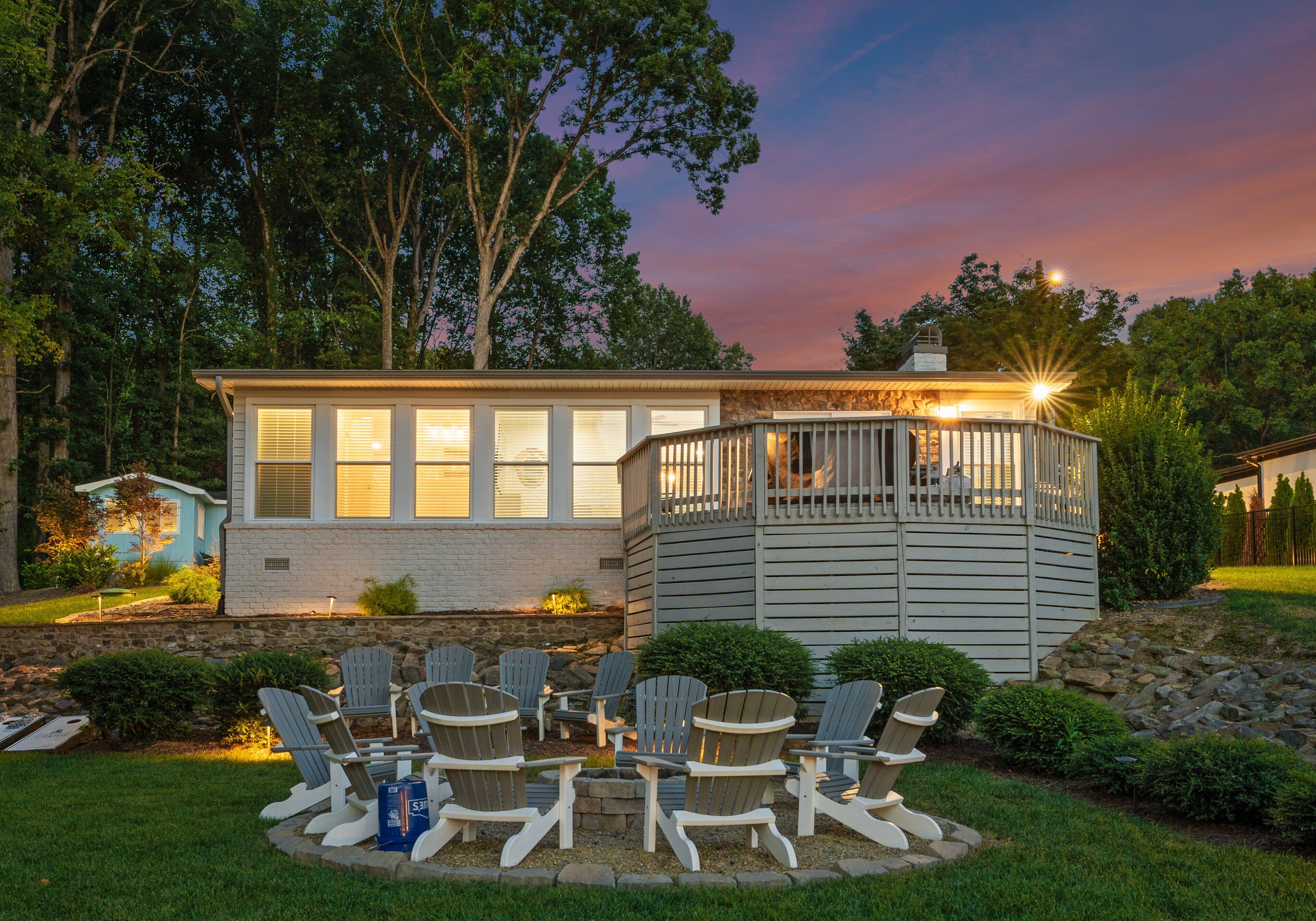 Une maison dotée d’une terrasse, entourée d’un jardin agrémenté de fauteuils Adirondack.