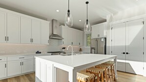 Una cocina moderna con armarios blancos, una isla central con taburetes y luminarias colgantes.