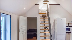 A compact kitchen with a white refrigerator, a microwave, and a small cabinet. A wooden ladder leads to a lofted sleeping area with a dark-colored sofa. - Gorgeous home in Villands with lake view (Villands)