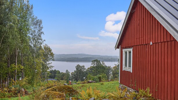 A red building with a window, surrounded by greenery and a lake. - Gorgeous home in Villands with lake view (Villands)