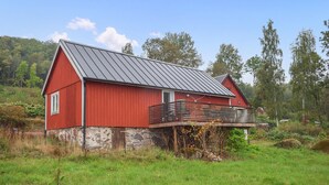 A red barn with a stone foundation, a metal roof, and a wooden deck. - Gorgeous home in Villands with lake view (Villands)