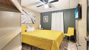 Ein Schlafzimmer mit Bett, Deckenventilator, Fernseher, Stuhl und Teppich mit Muster.