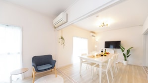 A modern living room with a white sofa, a dining table with chairs, a small round table, and a potted plant. - Miraie Yokkaichi Aobacho (Yokkaichi)