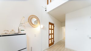 A modern interior with a white wall, a wooden door, a round mirror, and a floor lamp. - Miraie Yokkaichi Aobacho (Yokkaichi)