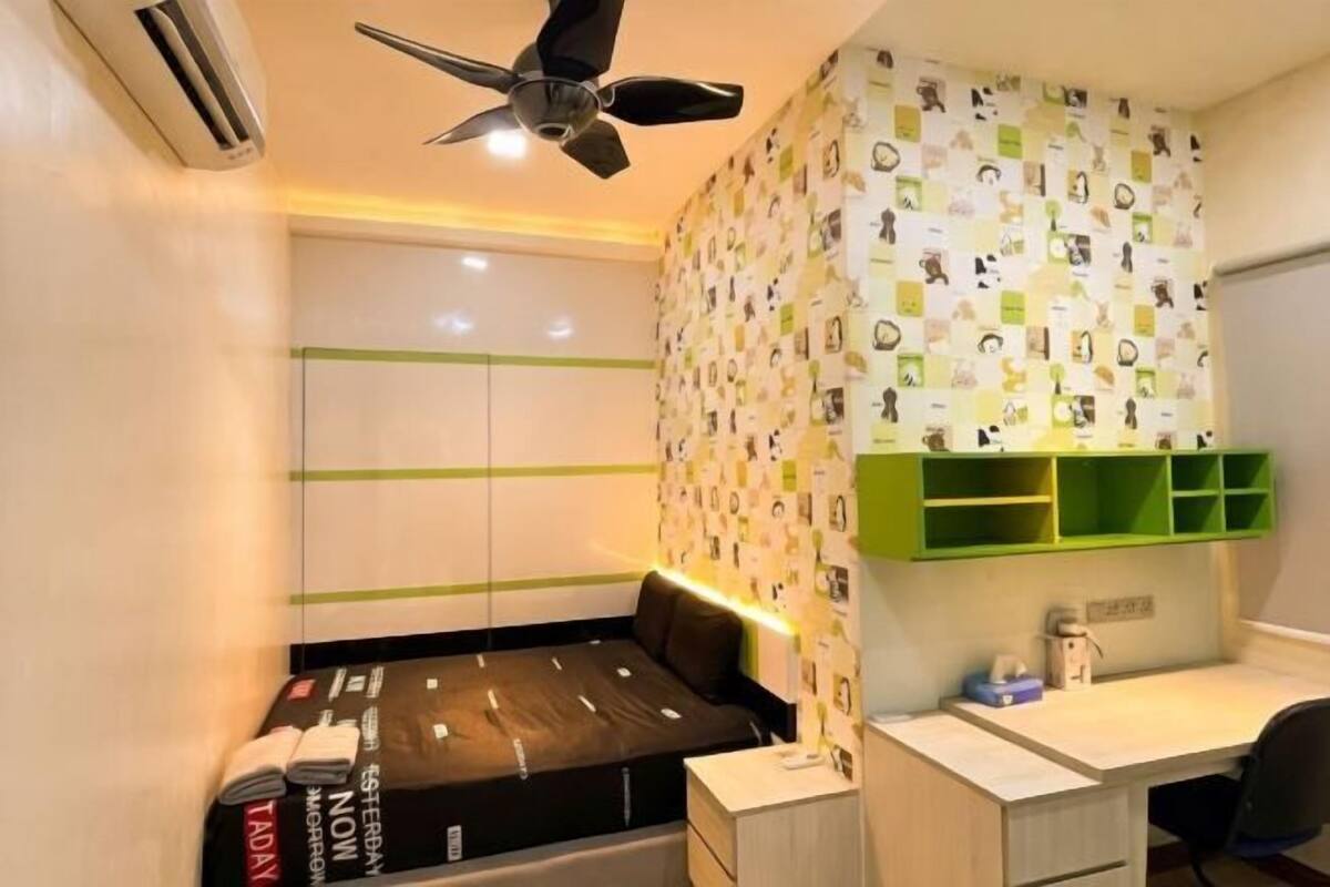 Une petite chambre comprenant un lit, un bureau et un ventilateur de plafond.
