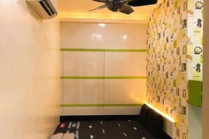 Ein Zimmer mit einem Bett, einer Wandklimaanlage, einem Deckenventilator und einer Wand mit ornamentalem Tapetenmuster.