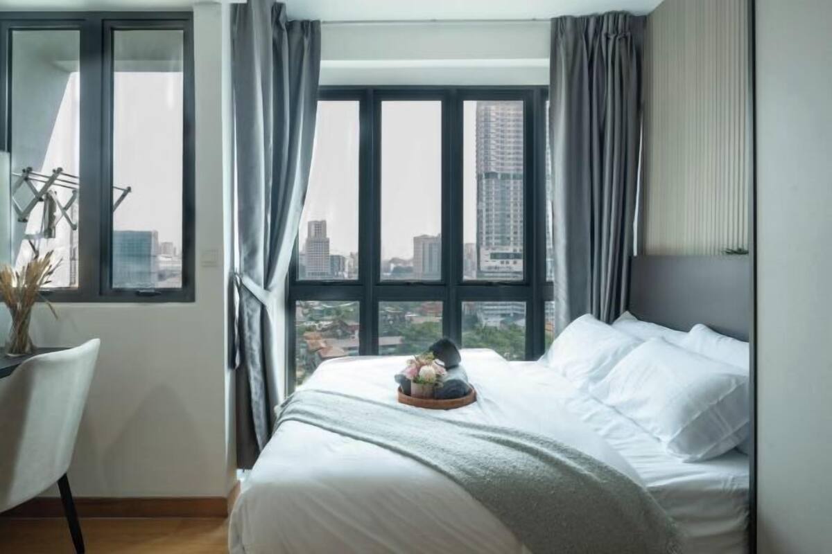 Hotelkamer met een groot bed, een stoel, een raam met gordijnen en uitzicht op de stad.